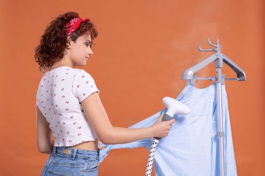 Ironing a man's shirt with an ironing steamer. A girl irons a shirt. Hot steam. Attractive woman with dark and curly hair.