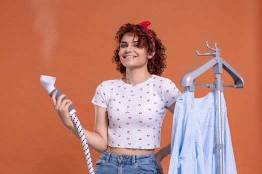 Smiling girl using a steamer to iron a man's shirt. Attractive girl with dark and curly hair. Hot steam.