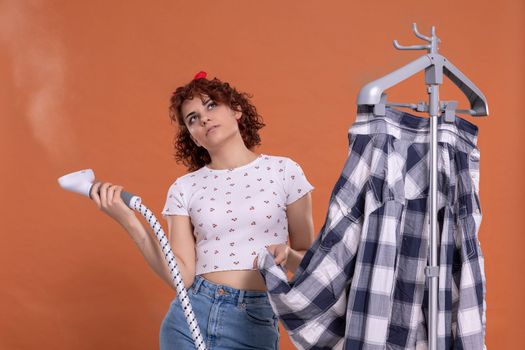 A woman is pondering and bubbling while ironing her shirt. Ironing steamer. Attractive girl with dark and curly hair. Hot steam.