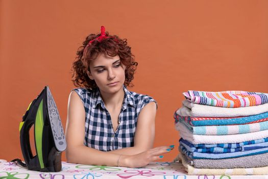 Ironed and folded towels in a fuzz. Tired girl with curly hair. Uniform brick-colored background. Isolated from the background.