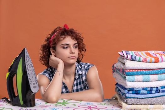 Ironed and folded towels in a fuzz. Tired girl with curly hair. Uniform brick-colored background. Isolated from the background.