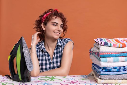 Full of joy and happiness, the girl with curly hair looks nonchalantly at the ironed towels lying on the ironing board.