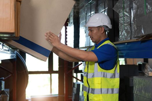 Smart millennial Asian male warehouse worker in his uniform working in warehouse, checking inventory in parcel. shipping warehouse job.