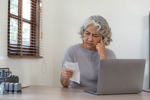Worried Senior woman having problem about Financial economic crisis. Stressed Asian Elderly male calculate family budget, Debts, monthly expenses with calculator and laptop computer at home.
