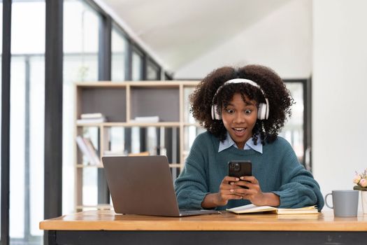 Photo of cheerful joyful mixed race woman playing games and wearing wireless headphones at home Play game on your smartphone that wins the moment of victory. Fun and enjoyable vacation.