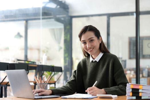Cheerful business lady working on laptop in office, Asian happy beautiful businesswoman in formal suit work in workplace. Attractive female employee office worker smile..