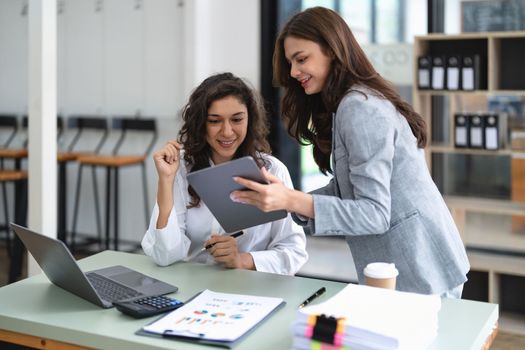 Diverse businesspeople cooperate work together discussing company financial statistics, multiracial colleagues collaborate brainstorm with finance on tablet