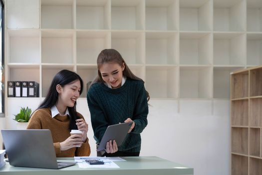 Two young Asian business woman talk, consult, discuss working with new startup project idea presentation analyze plan marketing and investment in the office...