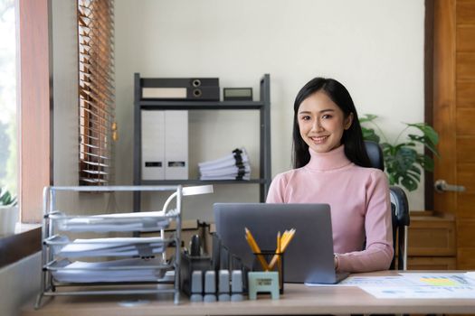 Asian woman using calculator and laptop for doing math finance on an office desk, tax, report, accounting, statistics, and analytical research concept..