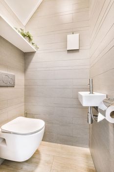 Interior of narrow restroom with sink and wall hung toilet with white walls and checkered floor