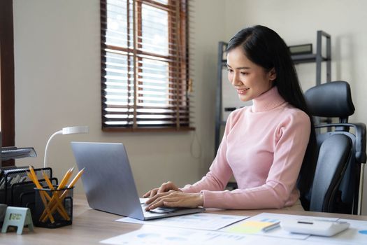 Asian woman using calculator and laptop for doing math finance on an office desk, tax, report, accounting, statistics, and analytical research concept..