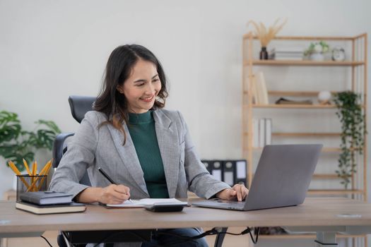 Asian Business woman using calculator and laptop for doing math finance on an office desk, tax, report, accounting, statistics, and analytical research concept..