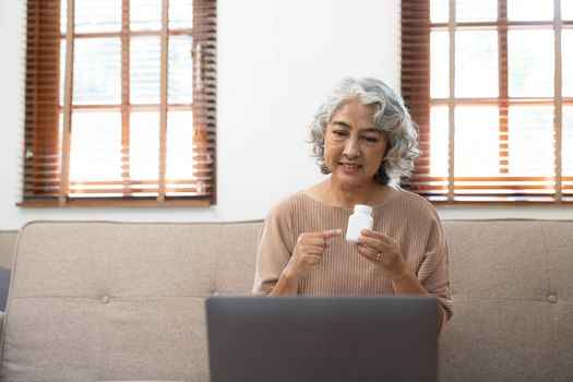 Asian seniors use laptop video conference with doctor about illness and prescription pill in living room at home.Healthy lifestyle.aging at home concept.