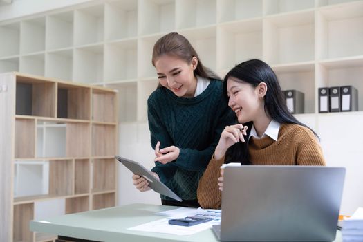 Two young Asian business woman talk, consult, discuss working with new startup project idea presentation analyze plan marketing and investment in the office...