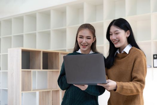 Two beautiful Asian businesswomen standing using digital tablet consulting and analyzing information in office work...