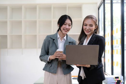 Two beautiful Asian businesswomen standing using digital tablet consulting and analyzing information in office work...