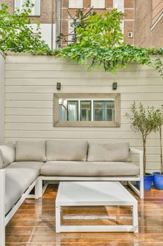 an outdoor living area with couches, coffee table and pots on the side of a building in the background