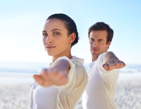 In balance with nature and ourselves. A young couple doing yoga on the beach