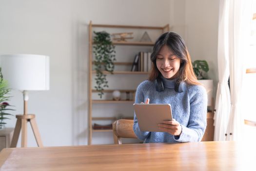 Happy young woman wearing headphone and using digital tablet at home