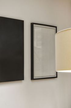 a black and white painting hangs on the wall next to a lamp in a room with two framed art pieces