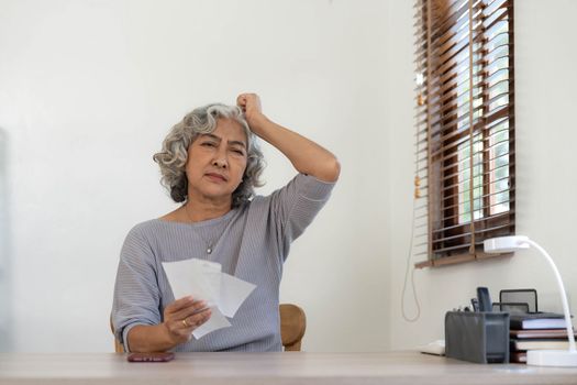 Worried Senior woman having problem about Financial economic crisis. Stressed Asian Elderly male calculate family budget, Debts, monthly expenses with calculator and laptop computer at home.