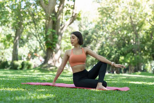 Young attractive girl is doing advanced yoga asana on the fitness mat in the middle of a park