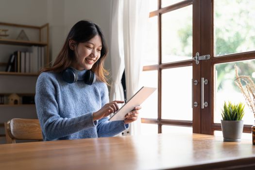 Happy young woman wearing headphone and using digital tablet at home