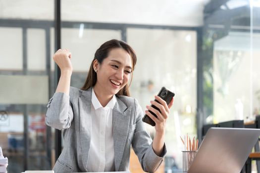 Excited happy Asian woman looking at the phone screen, celebrating an online win, overjoyed young asian female screaming with joy, isolated over a white blur background.