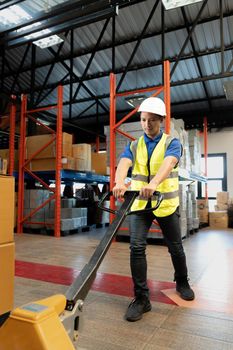 Portrait, Tired millennial Asian male warehouse worker pulling a pallet truck, suffering from back pain, working in warehouse