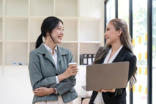 Two beautiful Asian businesswomen standing using digital tablet consulting and analyzing information in office work...