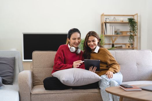 Asian woman friends sitting in living room watching movie on tablet together. Modern female friendship enjoy weekend activity lifestyle with wireless technology at home