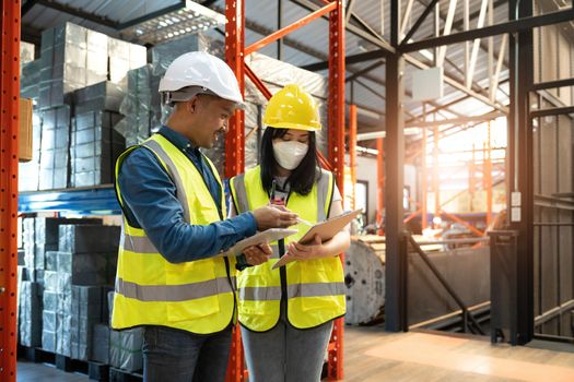 Professional adult Asian male warehouse manager and female worker are working together, checking their inventory in the warehouse or storehouse