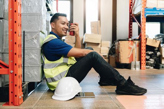 Asian male worker in safety uniform talking on walkie talkie to colleagues. engineer or driver working at logistic warehouse distribution center. shipping and delivery..