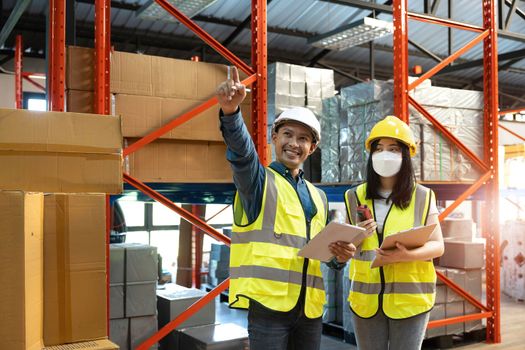 Professional adult Asian male warehouse manager and female worker are working together, checking their inventory in the warehouse or storehouse