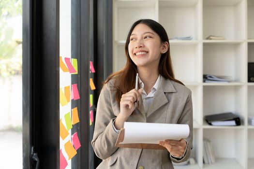 Portrait smile young asian woman making decisions thinking while at the office window