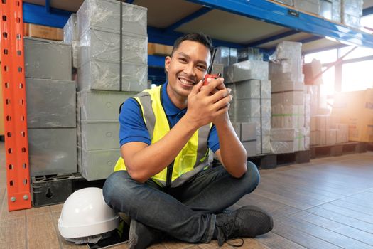 Asian male worker in safety uniform talking on walkie talkie to colleagues. engineer or driver working at logistic warehouse distribution center. shipping and delivery..