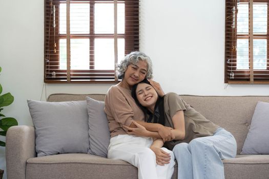 Portrait of Asian lovely family, young daughter hugging older mother. Attractive woman and senior elder mature mom sit on sofa, enjoy activity at home together in living room