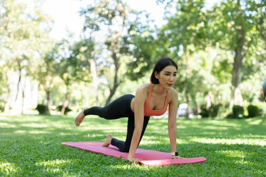 Young attractive girl is doing advanced yoga asana on the fitness mat in the middle of a park