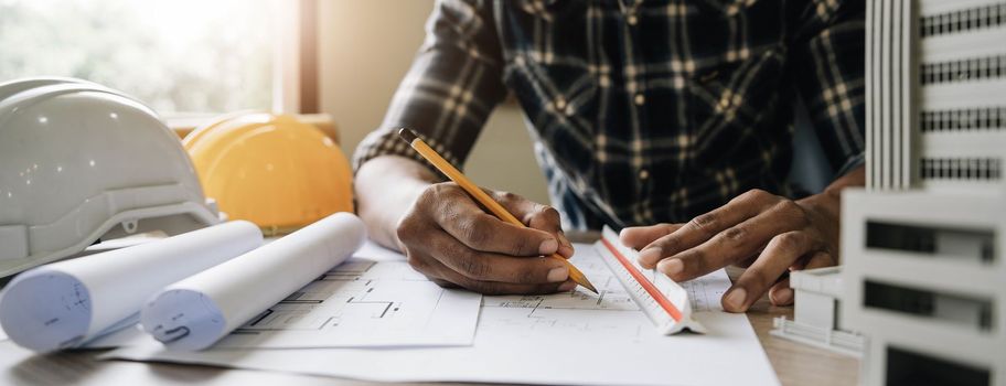 Image of engineer drawing a blue print design building or house, An engineer workplace with blueprints, pencil, protractor and safety helmet, Industry concept.