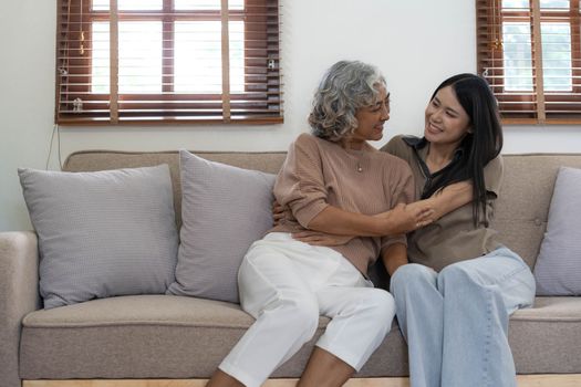 Portrait of Asian lovely family, young daughter hugging older mother. Attractive woman and senior elder mature mom sit on sofa, enjoy activity at home together in living room