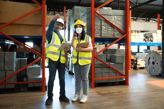 Professional adult Asian male warehouse manager and female worker are working together, checking their inventory in the warehouse or storehouse