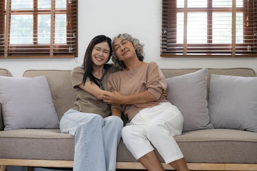 Portrait of Asian lovely family, young daughter hugging older mother. Attractive woman and senior elder mature mom sit on sofa, enjoy activity at home together in living room