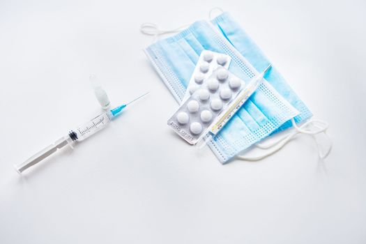 Preparation for vaccination against covid-19. Thermometer, pills, medical mask on a white table. Place for an inscription, horizontal photo