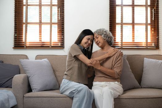 Loving adult daughter hugging older mother, standing behind couch at home, family enjoying tender moment together, young woman and mature mum or grandmother looking at each other, two generations..