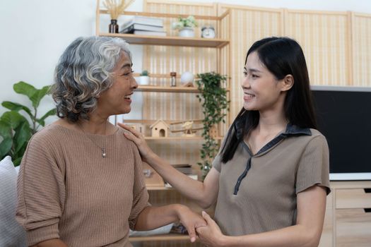 Portrait of Asian lovely family, young daughter hugging older mother. Attractive woman and senior elder mature mom sit on sofa, enjoy activity at home together in living room.