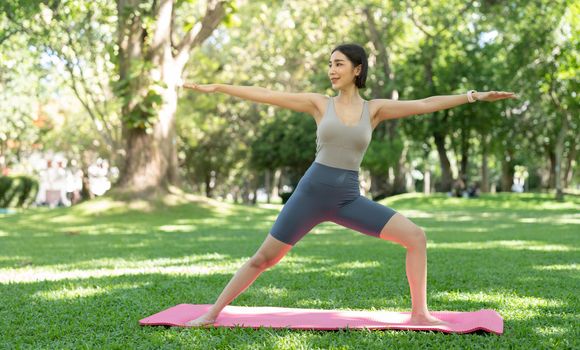 Young attractive girl is doing advanced yoga asana on the fitness mat in the middle of a park