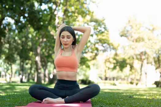 Young attractive girl is doing advanced yoga asana on the fitness mat in the middle of a park