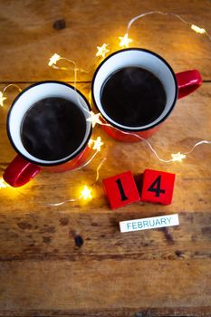 Two cups of coffee in red cups on a background of garlands. Postcard with date and month. Morning breakfast for Valentine's Day. Love concept