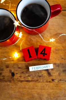 Two cups of coffee in red cups on a background of garlands. Postcard with date and month. Morning breakfast for Valentine's Day. View from above