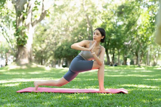 Young attractive girl is doing advanced yoga asana on the fitness mat in the middle of a park